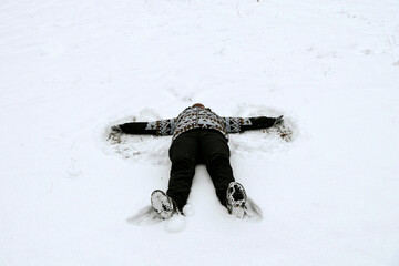 Adult making a snow angel on the snowy ground on a winter day.
