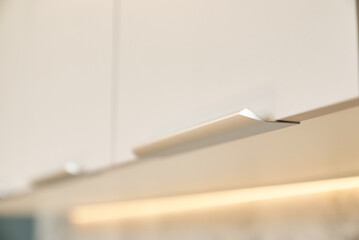 Close-up of contemporary white kitchen cabinets with integrated handle and lighting.