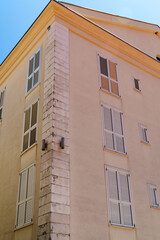 Obraz premium Low angle view of a pastel building facade with window shutters in Petrovac, Montenegro. Mediterranean architecture and summer sunlight.