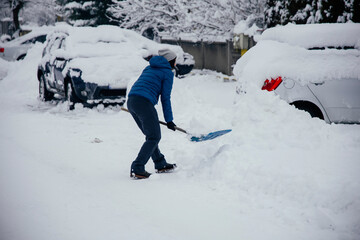 Woman removes snow near her car on a winter morning, outside his home in a residential area