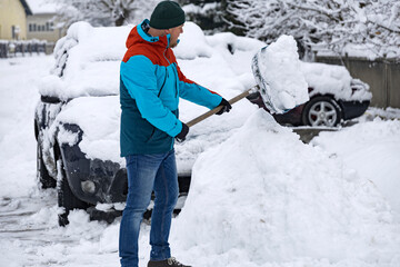 Man removes snow near car on a winter morning, outside his home in a residential area