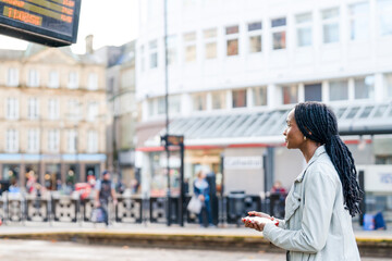 Waiting for the bus at a city stop while looking at the schedule board in the afternoon