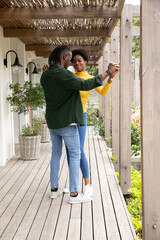 African american couple holding hands, dancing on wooden deck under pergola with lantern sconces © wavebreak3