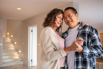 Senior couple holding hands and dancing at home near staircase lights and dining table © wavebreak3