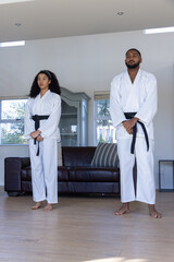 Fototapeta premium Diverse training partners practicing martial arts stance in living room wearing gis and belts