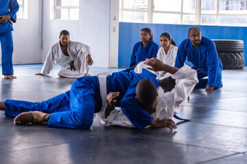 Diverse martial arts class in gis practicing ground grappling on mats in gym with tires