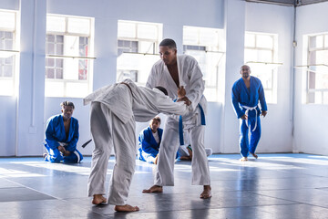 Male martial arts students grappling in bright dojo on padded mats with gis and belts