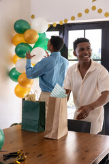 Obraz premium Diverse male friends decorating green gold balloons, arranging gift bags at home, copy space