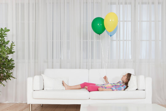 Child lying on white sofa holding balloons indoors in Munich