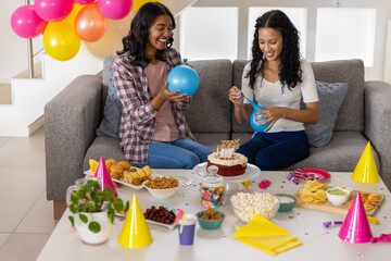 Diverse mom and teenage daughter sitting on sofa in living room sharing cake popcorn