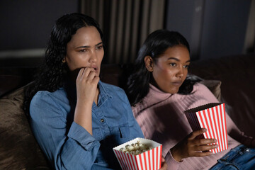Diverse female friends sitting on leather sofa in living room eating popcorn from striped boxes © wavebreak3