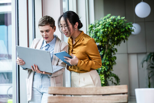 Two colleagues collaborating with laptop and tablet in modern office