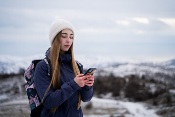 Calm Caucasian female traveler looking at the screen of smartphone in snowy mountains during daytime, hiker woman finds location during solo walk in nature outdoors, side view portrait
