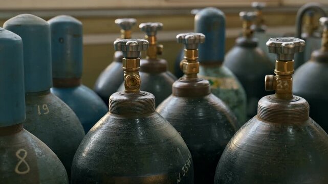 Industrial gas cylinders with valves stored in manufacturing facility. Gas supply, industrial storage and safety concept.