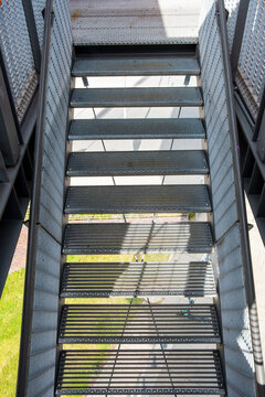 Industrial steel staircase with grating grid and vertical railing perspective in shadow guiding upward movement and determination forward