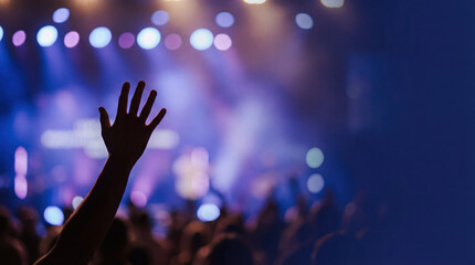 Silhouette of a hand raised in worship at a Christian concert or church service. Concept of praise, faith in God and spiritual surrender with blurred blue stage lights background.