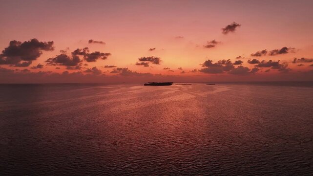 Aerial view of the tranquil ocean reflecting the vibrant hues of the sunset and distant islands, creating a serene landscape, Goidhoo, Baa Atoll, Maldives.