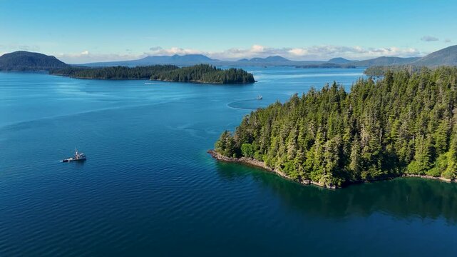 Aerial view of forested islands and a ship sailing through the shimmering waters, creating a stunning contrast of green and blue hues, Sitka, Alaska, United States.