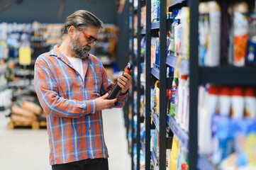 Portrait of focused man buying household chemicals in supermarket, reading labels on bottles