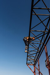 Freerunner balances on high steel. Male freerunner performs a daring balance move atop a tall metal beam during daytime parkour training at an outdoor structure under clear skies