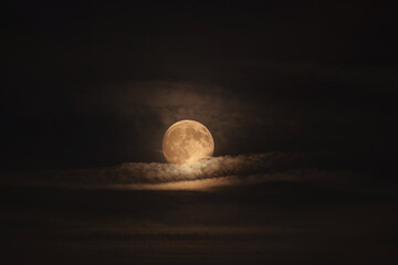 A luminous full moon rises through layered clouds, softly illuminating the night sky. The warm moonlight contrasts with dark tones, creating a serene and cinematic atmosphere
