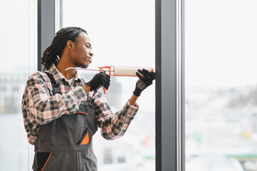 African American Construction worker applying silicone sealant to window frame