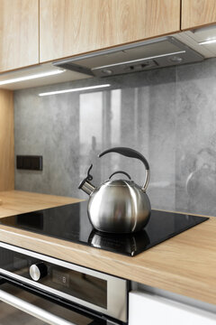 Photo of gray stainless steel kettle on the induction cooktop in the kitchen.
