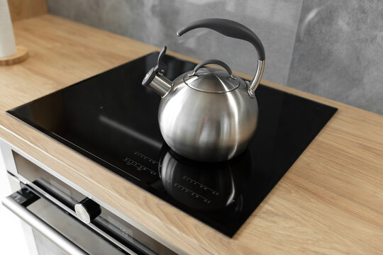 Photo of gray stainless steel kettle on the induction cooktop in the kitchen.