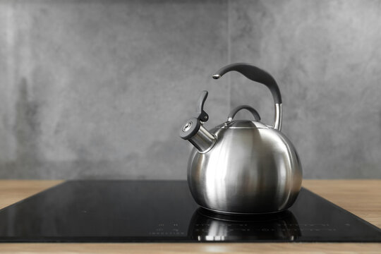 Photo of gray stainless steel kettle on the induction cooktop in the kitchen.