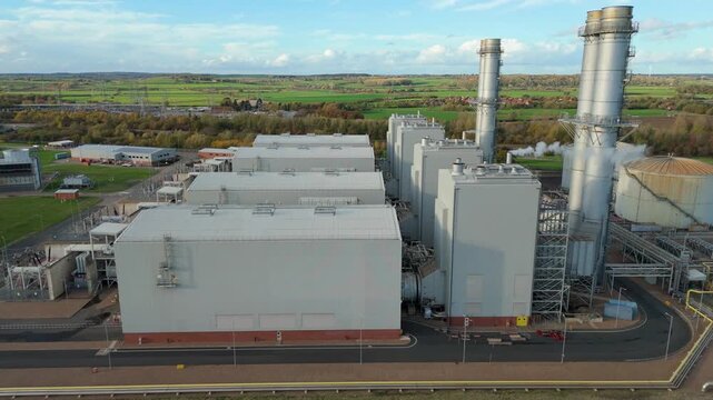 Drone aerial view of industrial gas power plant with turbines and cooling systems producing electricity at sunset in the UK