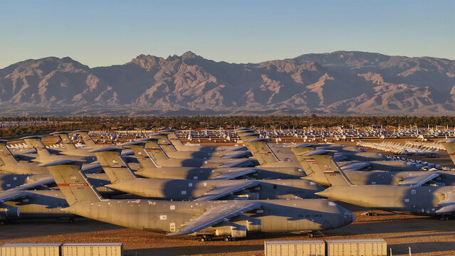 Aerial view of rows upon rows of military aircraft rest silently under the vast, open sky, framed by distant mountains, Tucson, Arizona, United States.