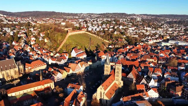 Medieval Esslingen city center unfolds in aerial perspective with Frauenkirche twin towers rising above historic Marktplatz and surrounding architecture, under bright clear blue sky, Germany