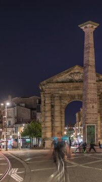 Porte d'Aquitaine arch and obelisk at Place de la Victoire night timelapse in Bordeaux, France. Illuminated landmark of historic Bordeaux with tram lines, cafes and lively surrounding