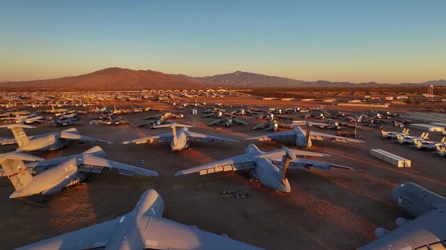 Aerial view of row upon row of retired military aircraft sit in the Arizona desert, their metallic bodies reflecting the warm glow of the setting sun, Tucson, Arizona, United States.