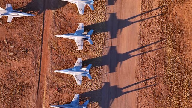 Aerial view of a fleet of fighter jets casting long shadows on the arid desert landscape and dirt runway, Tucson, Arizona, United States.