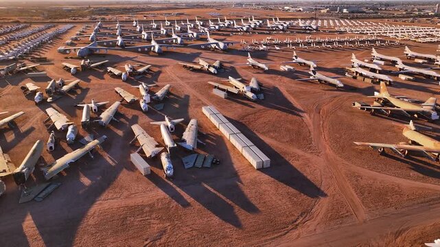 Aerial view of rows of retired aircraft glinting in the sun's warm glow against the red desert earth, Tucson, Arizona, United States.