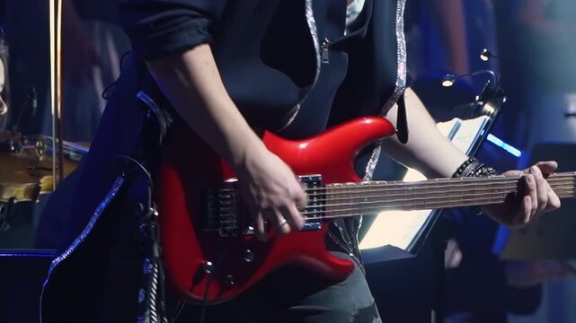 Musician intensely plays bright red electric guitar on stage with body angled. Stage lighting casts energetic glow enhancing atmosphere