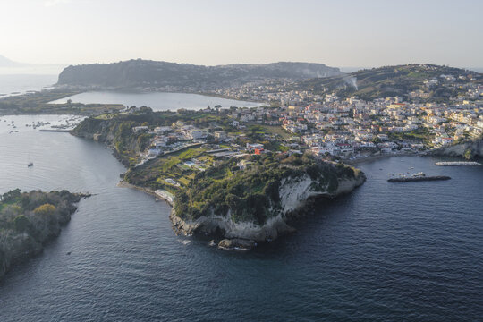 Aerial view of the peninsula where deep blue waters meet the verdant land, contrasting with the bright buildings of the town, Capo Miseno, Bacoli, Italy.