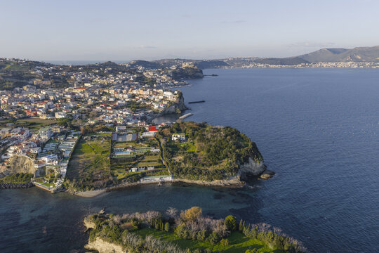 Aerial view of the tranquil waters meeting the rugged coastline and the vibrant town on the hillside, Capo Miseno, Bacoli, Campania, Italy.