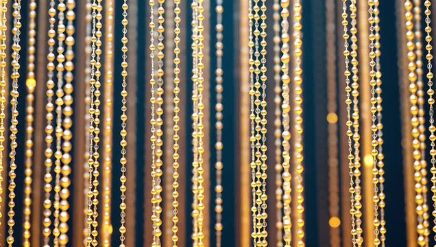 Decorative arrangement of gold and white beads or pearls hanging vertically on a dark background, reflecting light