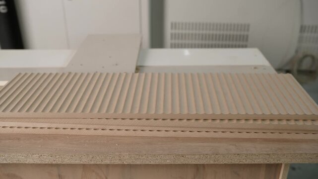 Detailed view of stacked mdf boards with a decorative linear pattern, freshly cut by a cnc router in a modern furniture manufacturing plant