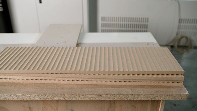 Detailed view of stacked mdf boards with a decorative linear pattern, freshly cut by a cnc router in a modern furniture manufacturing plant
