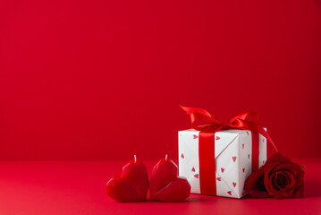 Gift, present box decorated with red ribbon and hearts, red rose flowers, heart shaped candles on red background. Valentine's day, 14 February, birthday, 8 march women's day gift. Love and romance.