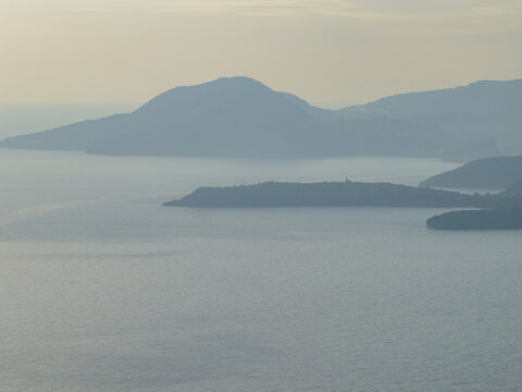 Aerial view of calm waters reflecting the soft light of the sky, with distant land masses fading into the horizon, Procida, Campania, Italy.
