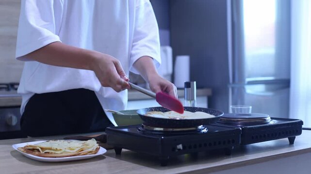 Watch a skilled cook expertly flip and cook a delicate crepe in a non-stick pan. Using a pink spatula, they ensure even browning while maintaining the crepes tender texture. Ideal for breakfast