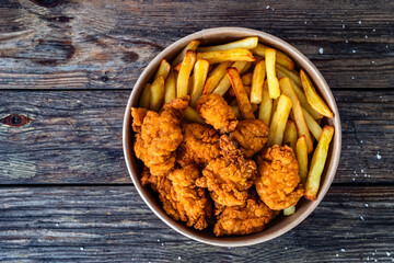 Takeaway breaded chicken nuggets with French fries on wooden table. Top view