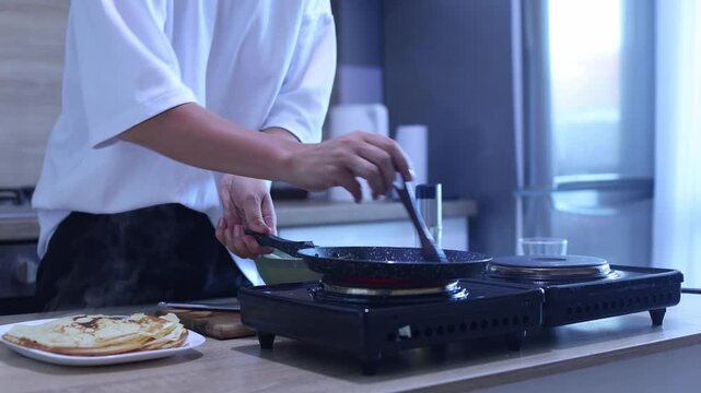 Watch as a cook pours smooth crepe batter into a hot pan and swirls it for an even, thin layer. A simple yet essential technique for flawless, golden crepes every time.