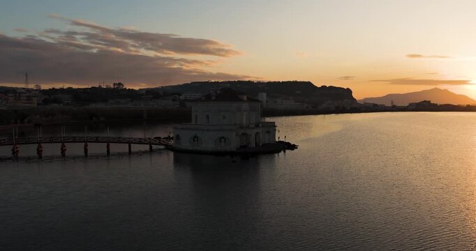 Aerial view of Casina Vanvitelliana over the calm waters during golden hour, contrasting the building's pale facade, Fusaro Lake, Bacoli, Italy.