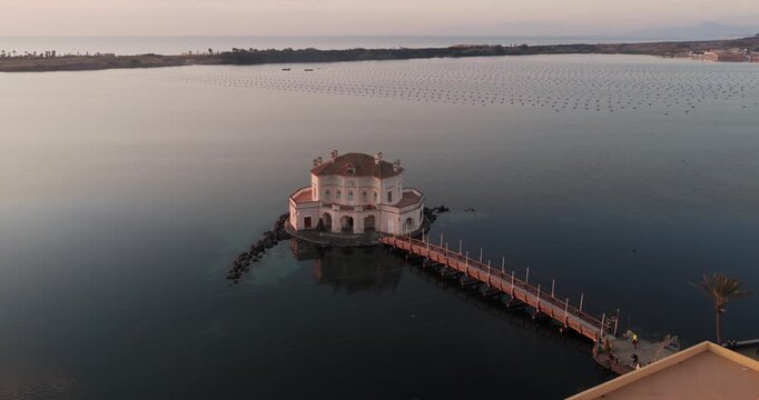 Aerial view of Casina Vanvitelliana standing out against the dark water, with a wooden bridge connecting it to the shore, Fusaro Lake, Bacoli, Italy.