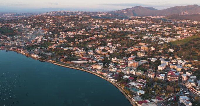 Aerial view of the town along the coastline, where buildings meet the tranquil waters of Fusaro Lake, Bacoli, Campania, Italy.